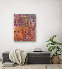 Load image into Gallery viewer, Aboriginal multicolored painting on a white wall above a gray ottoman with a plant and books.