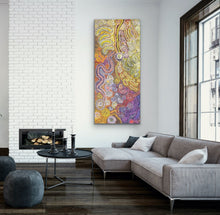 Load image into Gallery viewer, Living room with a colorful Aboriginal painting painting on a white brick wall, gray sectional sofa, and a fireplace.
