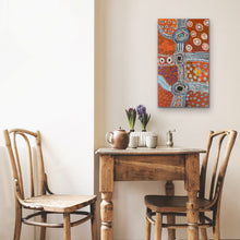 Load image into Gallery viewer, Small wooden table with two chairs and a colorful Aboriginal painting on the wall.
