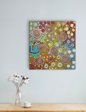 Load image into Gallery viewer, Colorful Aboriginal artwork on a wall above a wooden table with a vase and cup.
