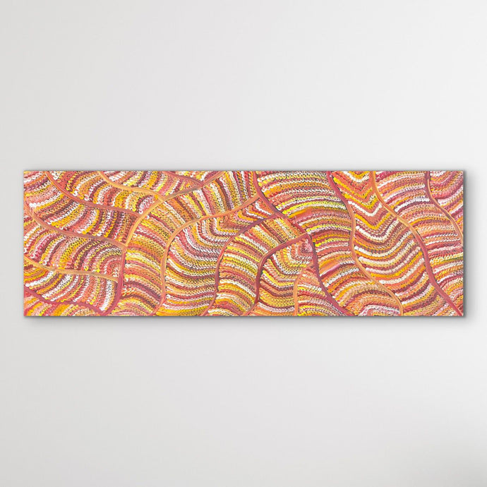 Aboriginal dot painting sand dunes vertical view with orange, red and yellow shown on white wall.