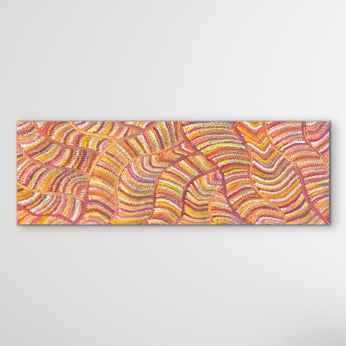 Aboriginal dot painting sand dunes vertical view with orange, red and yellow shown on white wall.